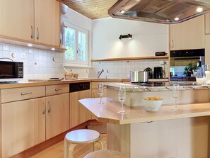 A modern kitchen with wooden cabinets, a microwave, a coffee maker, and a glass of wine on the counter.