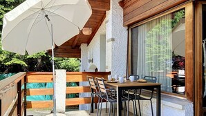 An outdoor patio with a table and chairs, a white umbrella, and a view of a pool and greenery. - Cosy apartment in villa for 4 guests with WIFI, terrace and pets allowed (Châtel-saint-denis)