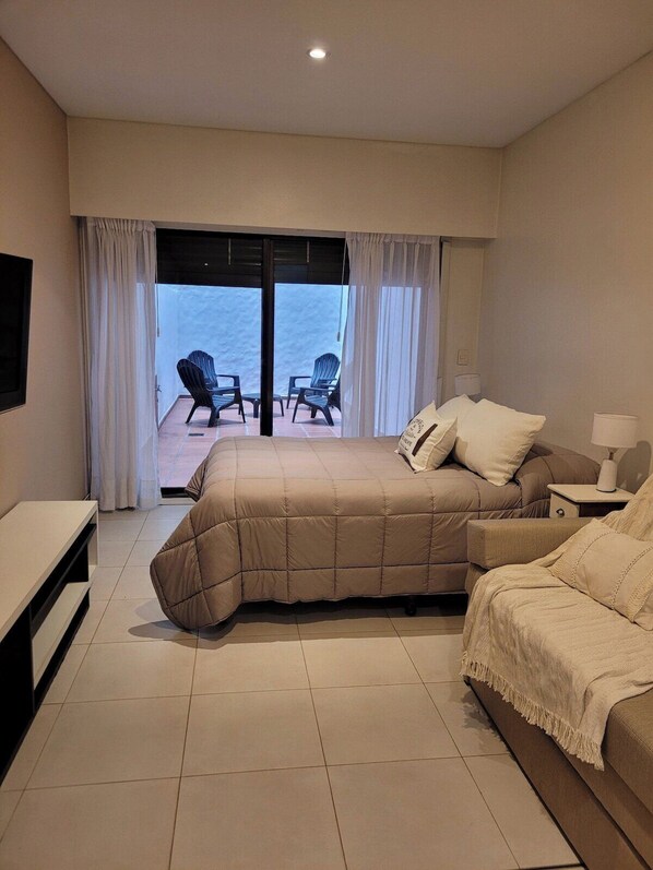 A hotel room with a bed, a sofa, a TV, and a balcony with chairs. - Recoleta Apartment with a Spacious Patio (Buenos Aires)