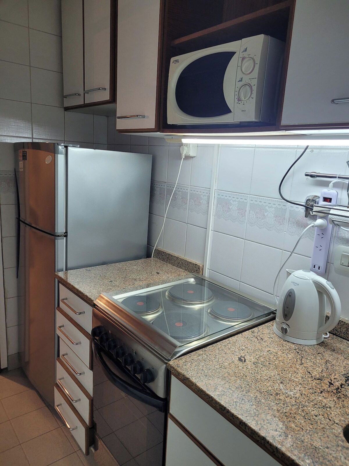 A kitchen with a stainless steel refrigerator, a microwave, a stove, and a kettle.