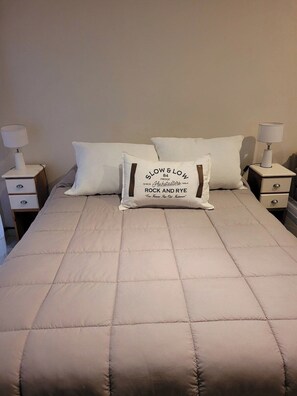 A bed with a beige quilted bedspread, two white pillows, and two bedside tables with lamps. - Recoleta Apartment with a Spacious Patio (Buenos Aires)