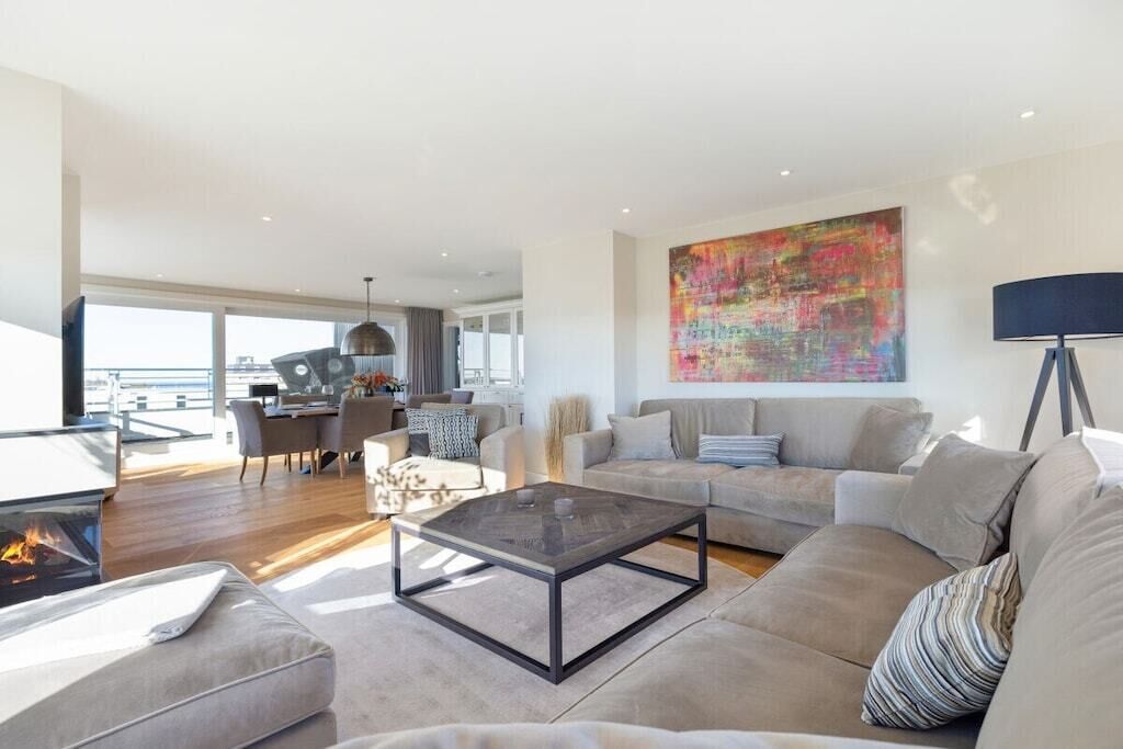 A spacious living room with a fireplace, a large abstract painting, and a dining area with natural light.