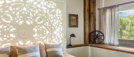 A bedroom with a bed, a window with curtains, a wall-mounted lamp, and a decorative wheel.