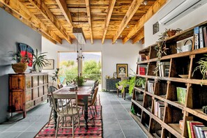 A dining area with a wooden ceiling, a large window, and a bookshelf filled with books. - The Windbourne A Luxury Retreat In The Catskills (Saugerties)