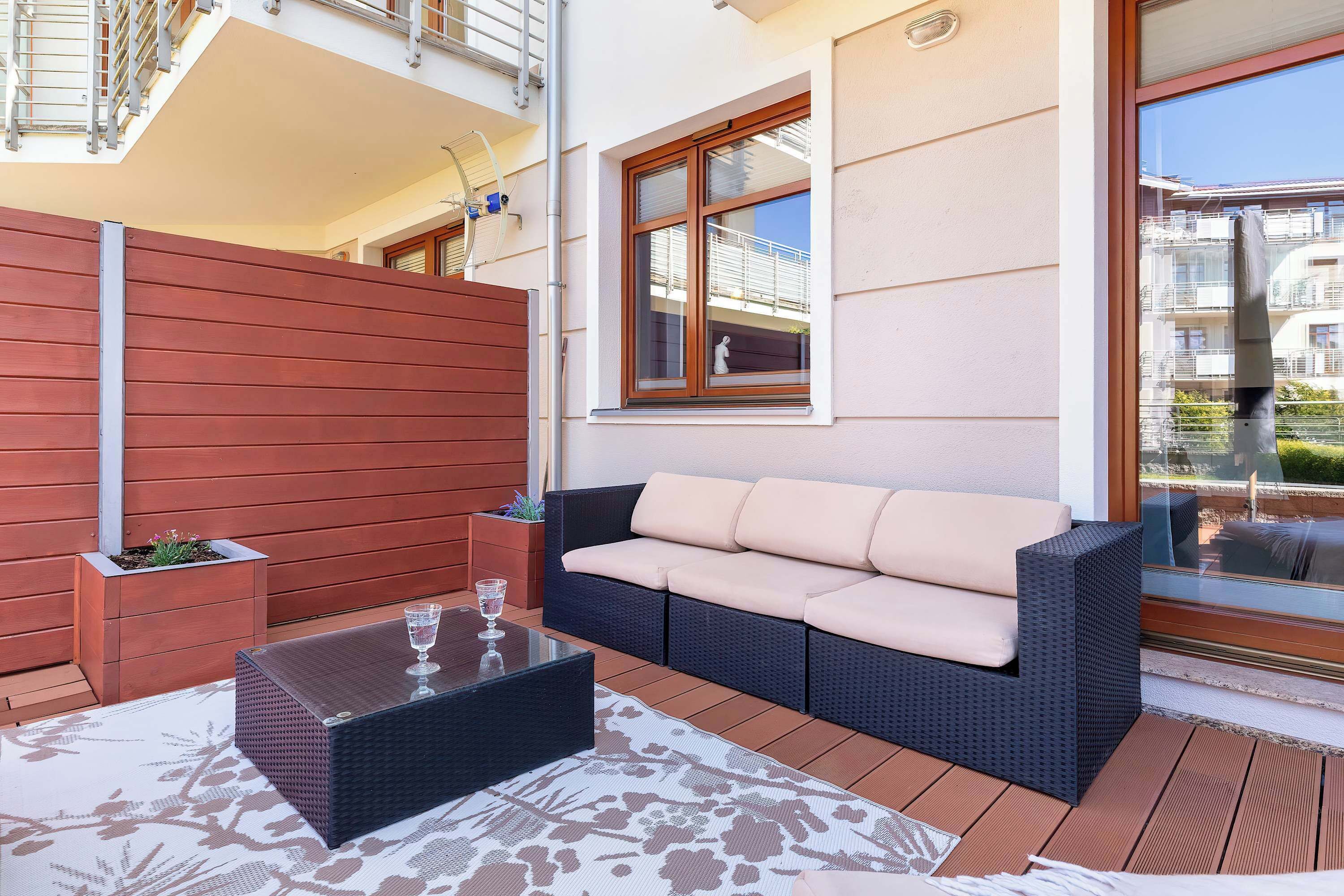 Un balcon avec un canapé en osier, une table basse en verre et une plante en pot.