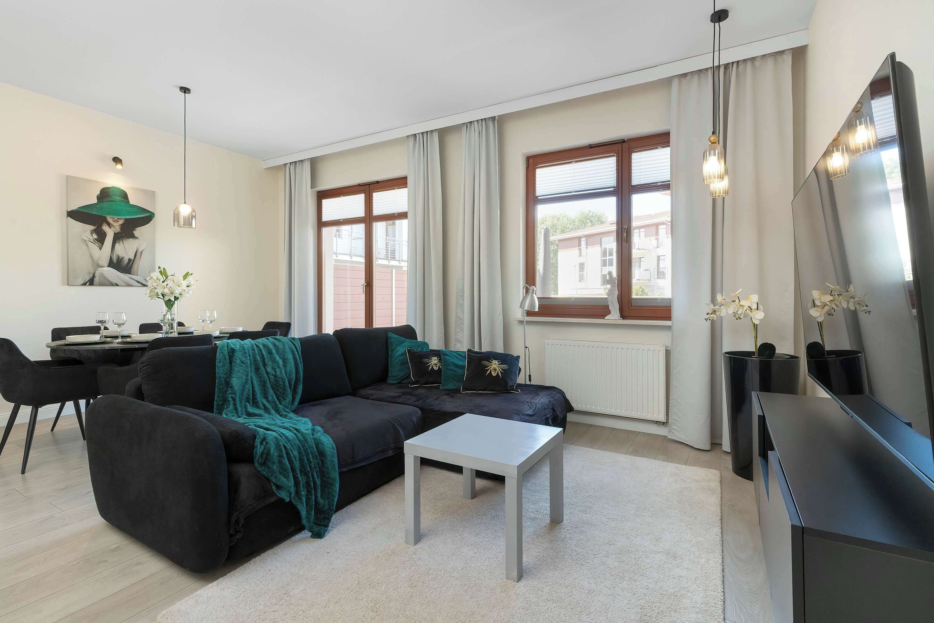 A modern living room with a black sofa, a white coffee table, and a dining area with a table set for two.