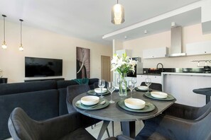 A modern dining area with a round table, black chairs, and a minimalist kitchen in the background. - Spacious Vervena Apartment with Terrace | Close to the Beach (Gdańsk)