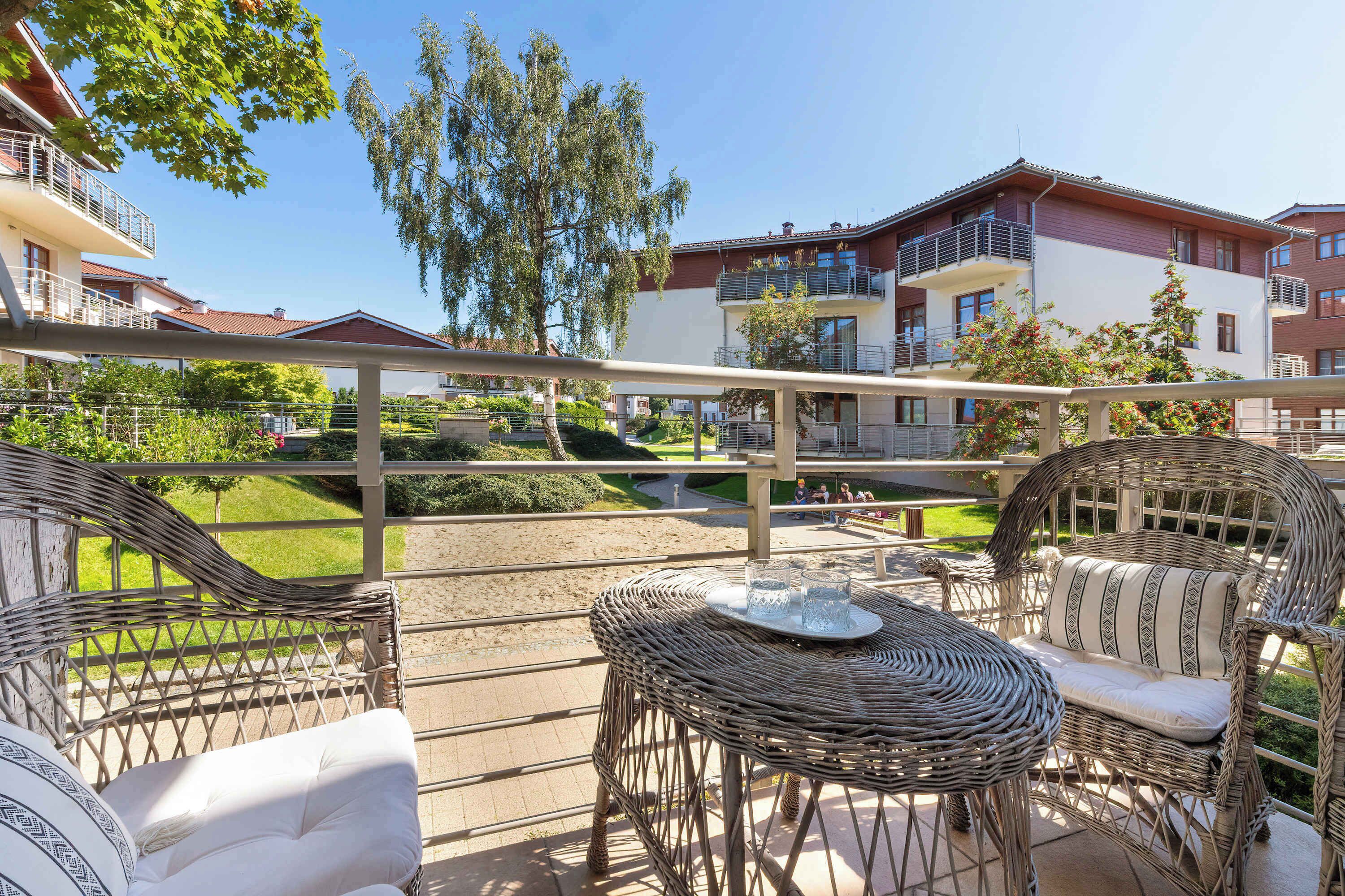 A balcony with wicker furniture, a table with glasses, and a view of buildings and greenery.