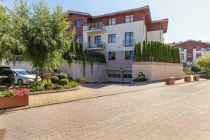A multi-story residential building with a balcony, a garage, and a landscaped garden with various plants and flowers. - Spacious Vervena Apartment with Terrace | Close to the Beach (Gdańsk)