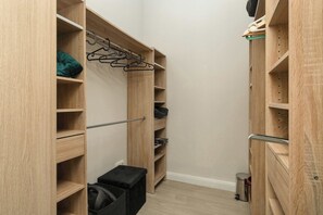Ein schmaler begehbarer Kleiderschrank mit Holzregalen, einer Kleiderstange und einer kleinen Ablagebank.