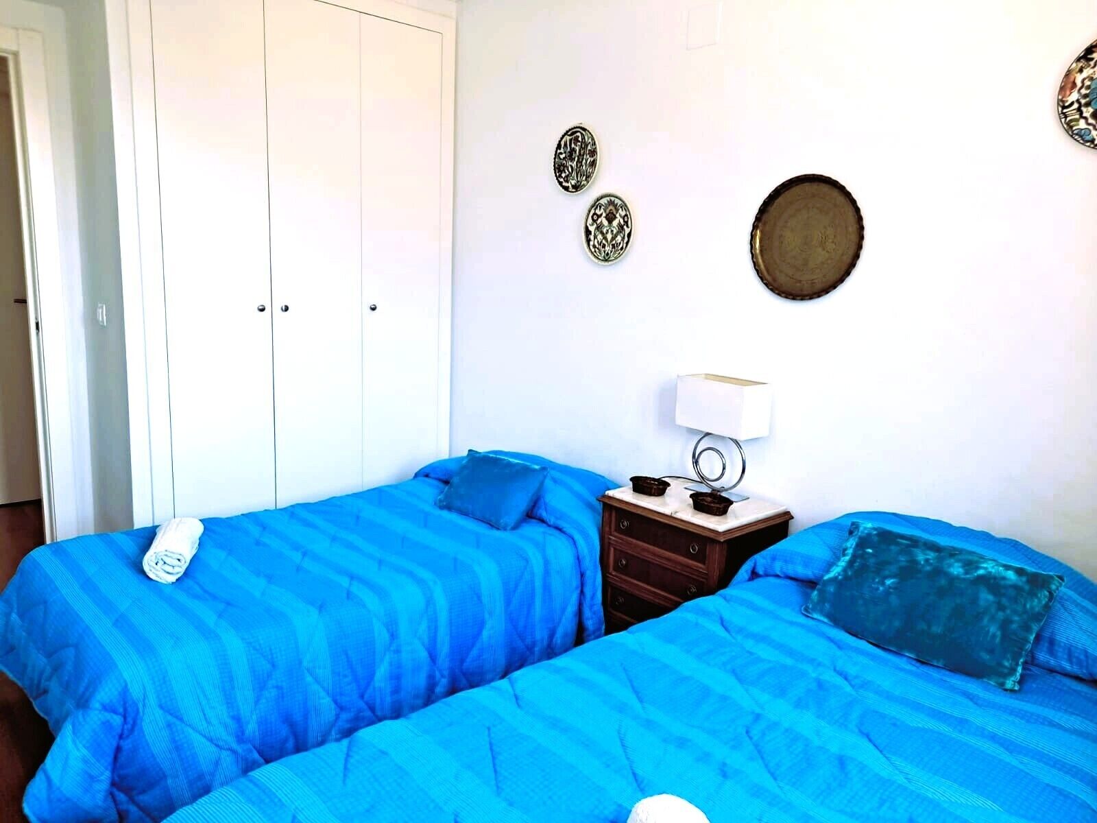 Une chambre avec deux lits, une table de chevet avec une lampe et un mur décoré d’assiettes.