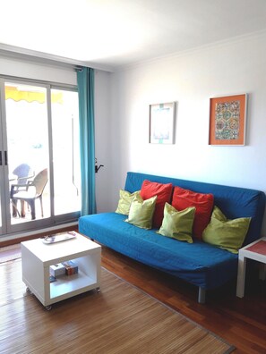Ein Wohnzimmer mit einem blauen Sofa, einem weißen Couchtisch und einer Glasschiebetür, die zu einem Außenbereich führt.