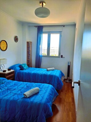 Een slaapkamer met twee bedden, een raam, een plafondventilator en een nachtkastje.