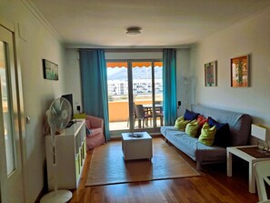 Een woonkamer met een bank, een bijzettafeltje, een ventilator en uitzicht door een glazen deur.