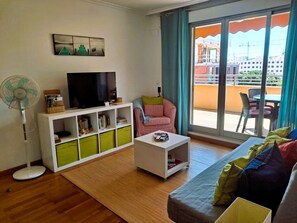 Ein Wohnzimmer mit Fernseher, Ventilator, Sofa und Blick auf einen Balkon.