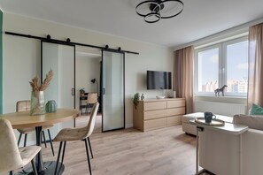 Ein modernes Wohnzimmer mit einer Schiebetür, einem Flachbildfernseher, einem Essbereich mit Stühlen und Blick auf Gebäude durch das Fenster.