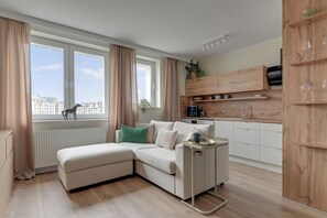 A modern living room with a sectional sofa, a small side table, and a view of the city through large windows. - Gdansk Riverside - Kamienna Grobla 24  (Gdańsk)