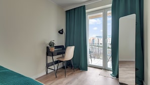 Un dormitorio moderno con un escritorio, una silla y vista a la ciudad a través de un ventanal grande.