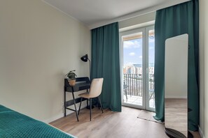 A modern bedroom with a desk, chair, and a view of the city through a large window. - Gdansk Riverside - Kamienna Grobla 24  (Gdańsk)