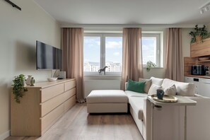 A modern living room with a sofa, a TV, and a view of buildings through large windows. - Gdansk Riverside - Kamienna Grobla 24  (Gdańsk)