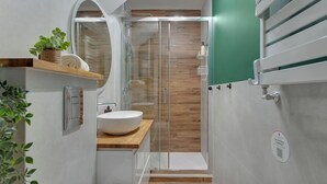 Un baño pequeño con un lavabo blanco, tocador de madera y cabina de ducha de vidrio.