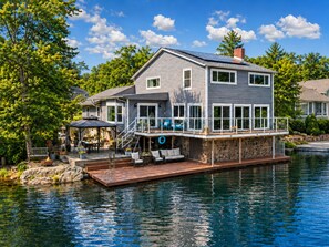 Ein Haus am Wasser mit Terrasse, Sitzgelegenheit im Freien und einem Swimmingpool.