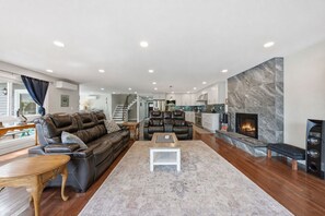 A spacious living room with a fireplace, leather sofas, and a dining area with a wooden table. - Lakefront Retreat | Game Room • Pizza Oven (Hewitt)