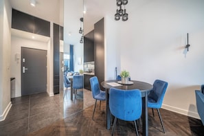 A modern dining area with a round table and blue chairs, a dark wood floor, and a ceiling with pendant lighting. - Apartment Żelazna 58 (Warszawa)