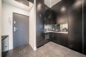 A modern kitchen with dark cabinetry, a built-in oven, and a stainless steel countertop. - Apartment Żelazna 58 (Warszawa)