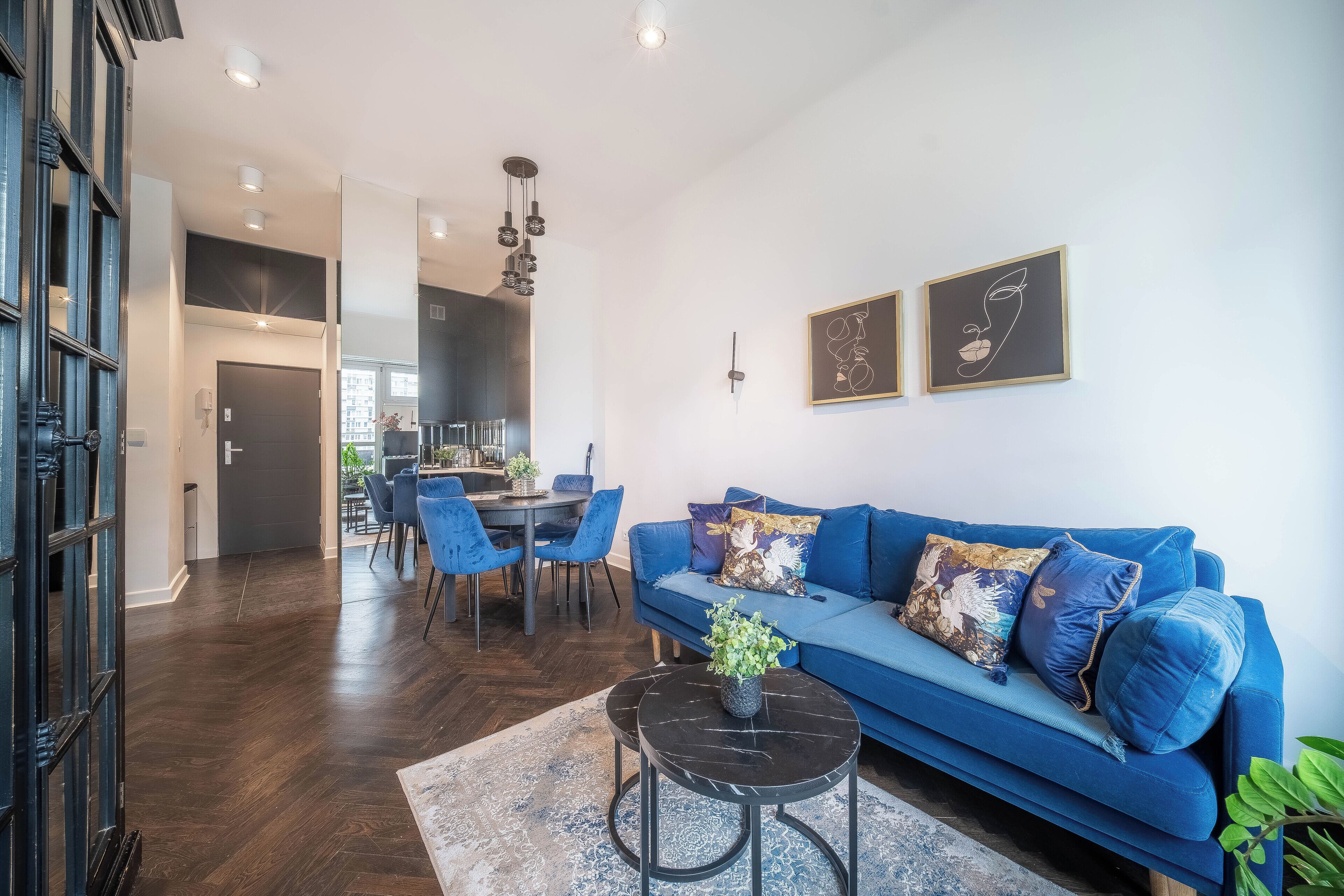 Uma sala de estar moderna com um sofá azul, uma área de jantar com cadeiras e uma cozinha ao fundo.