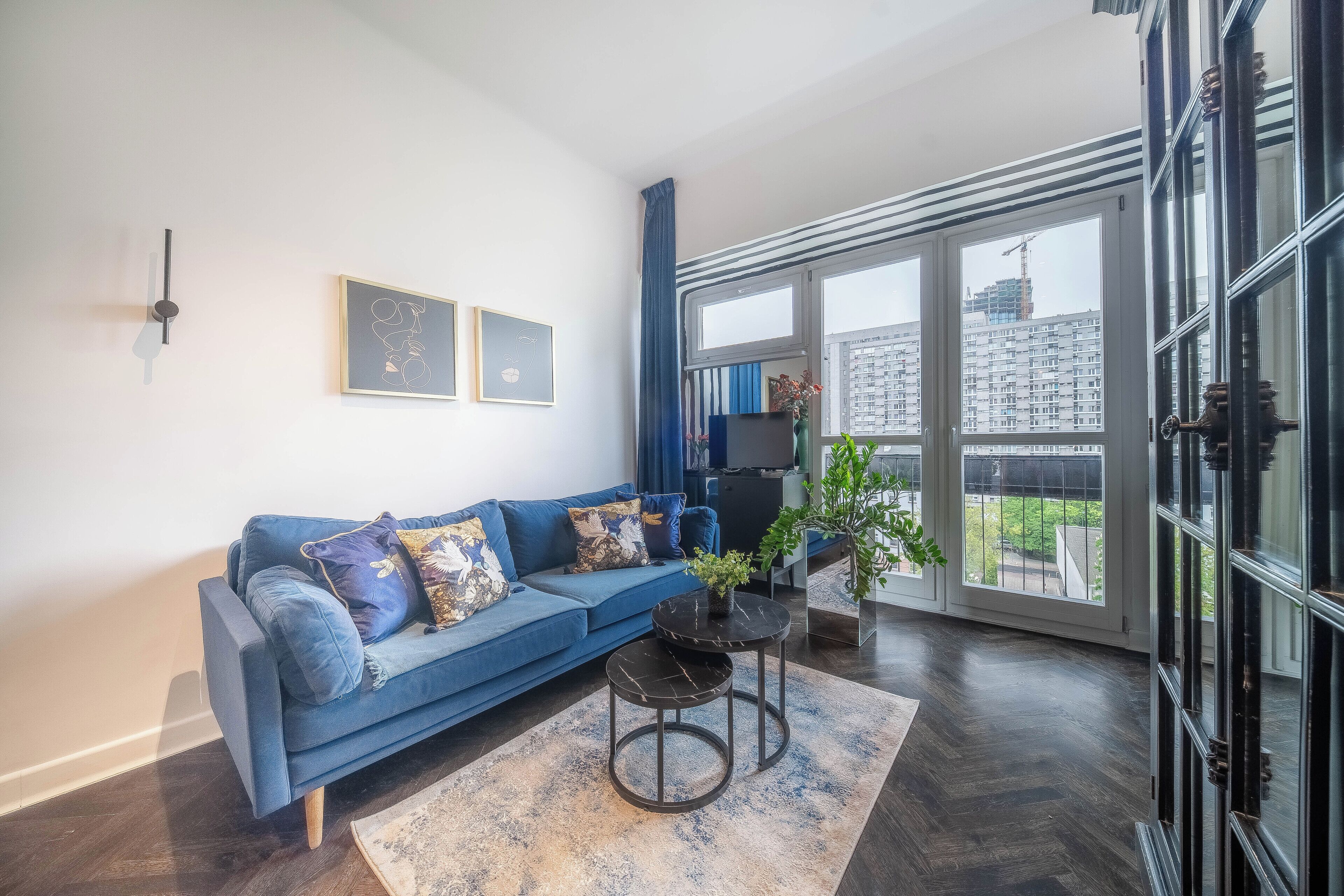 A modern living room with a blue sofa, a coffee table, and a large window with a view of buildings.