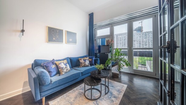 Una sala de estar moderna con un sofá azul, una mesa de centro y un ventanal con vistas a edificios.