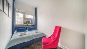 Un dormitorio con cama, ventana, una silla y vistas a un edificio.