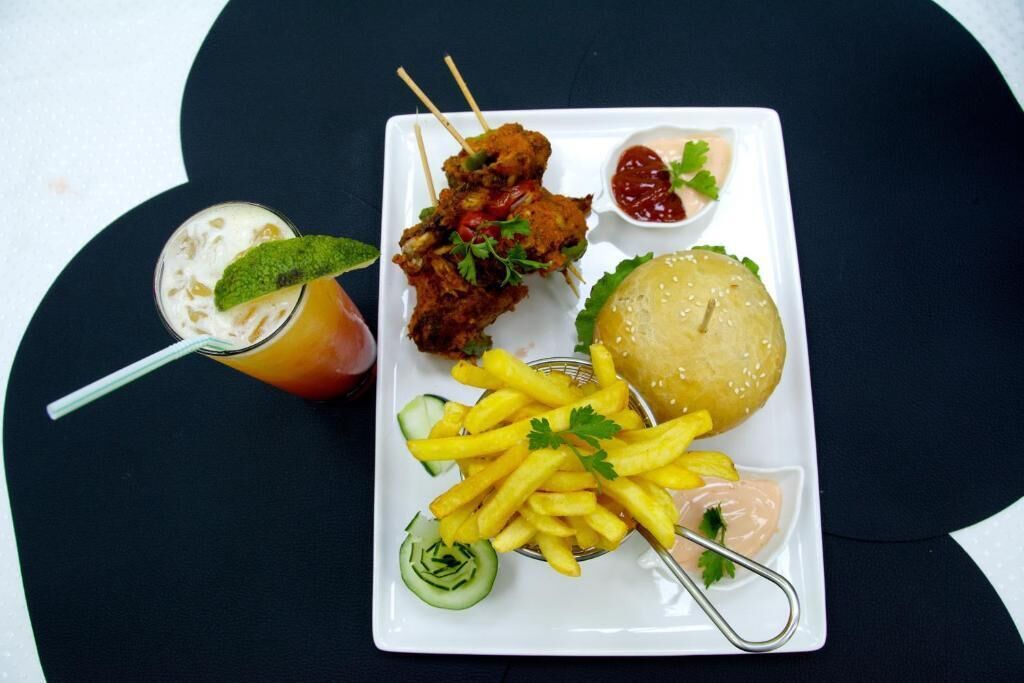 Een maaltijd bestaande uit gefrituurde kip, friet, een hamburger en een drankje met rietje.