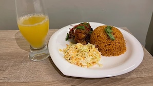 Un plato con arroz, un alimento frito y ensalada de col, acompañado de un vaso de jugo de naranja.