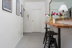 Un couloir avec une porte blanche, des tableaux encadrés accrochés au mur, un miroir et une table avec des tabourets.