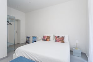 Een slaapkamer met een bed, nachtkastje, lamp, wandplank en een deur naar de badkamer.