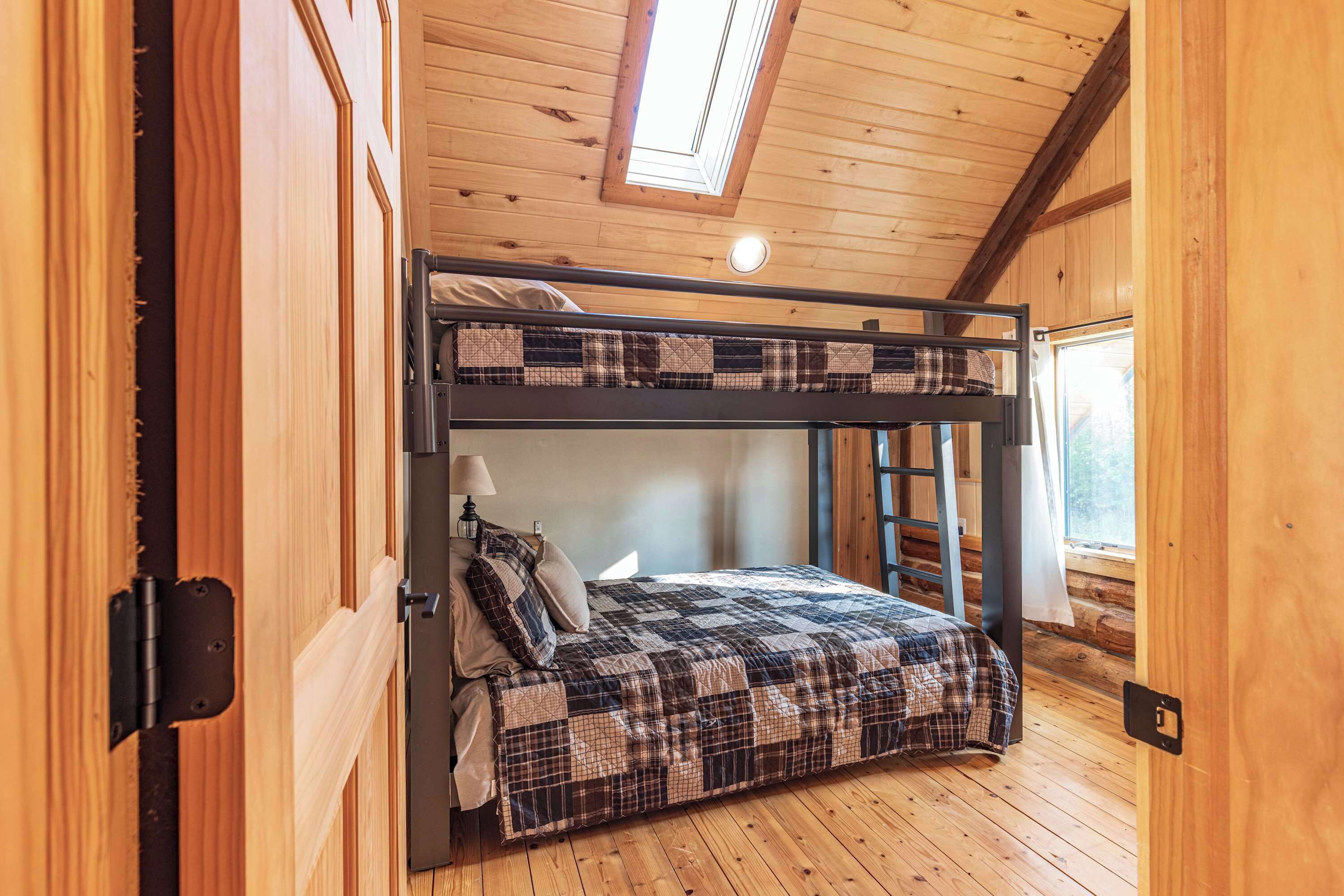 A bunk bed with a plaid quilt, a window with a view, and a skylight.