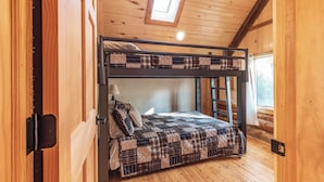 Un lit superposé avec une couette à carreaux, une fenêtre donnant sur un beau paysage et une lucarne.