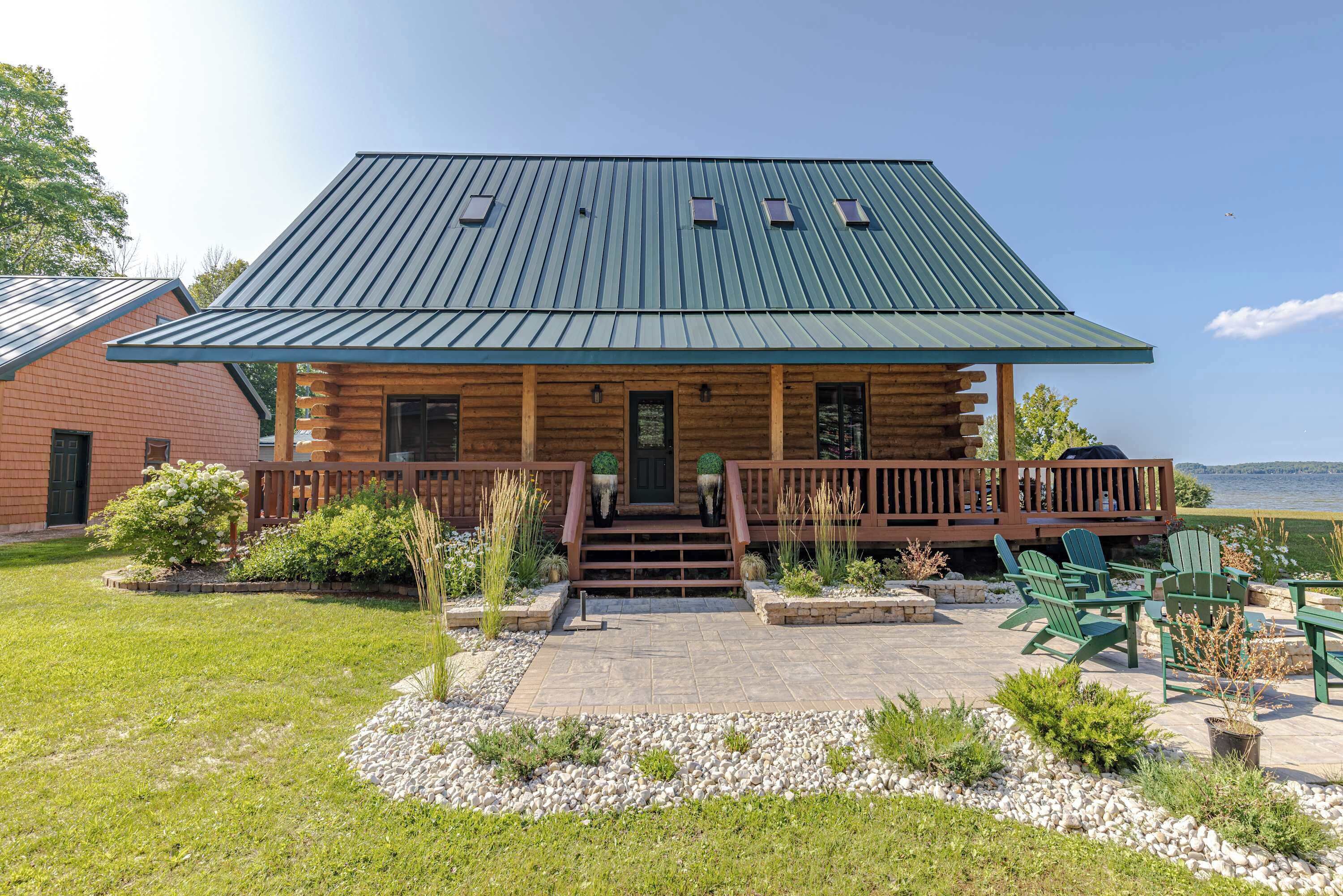 A log cabin with a metal roof, a front porch with steps, and a view of a lake.