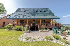 A log cabin with a metal roof, a front porch with steps, and a view of a lake. - Lakefront Log Cabin | Private Dock, Beach, Firepit (Curtis)