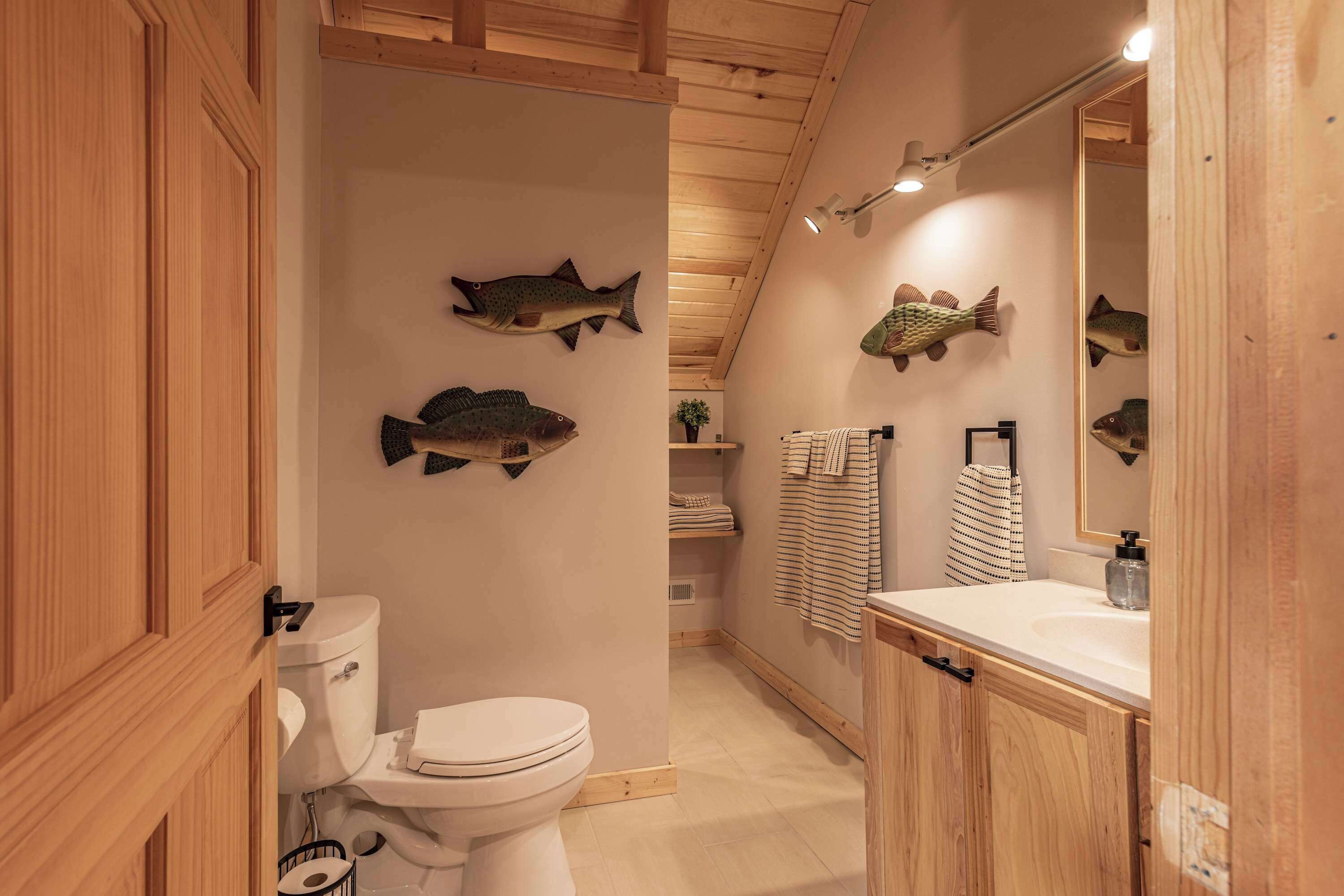 Ein Badezimmer mit Holzwänden, einer Toilette, einem Waschbecken mit Spiegel und Fisch-Wandbildern.
