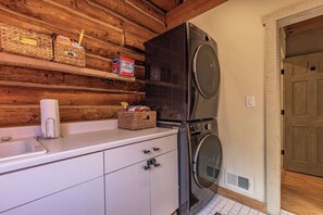 Une petite cuisine équipée d’un lave-linge, d’un évier et d’étagères en bois où sont rangés divers objets.