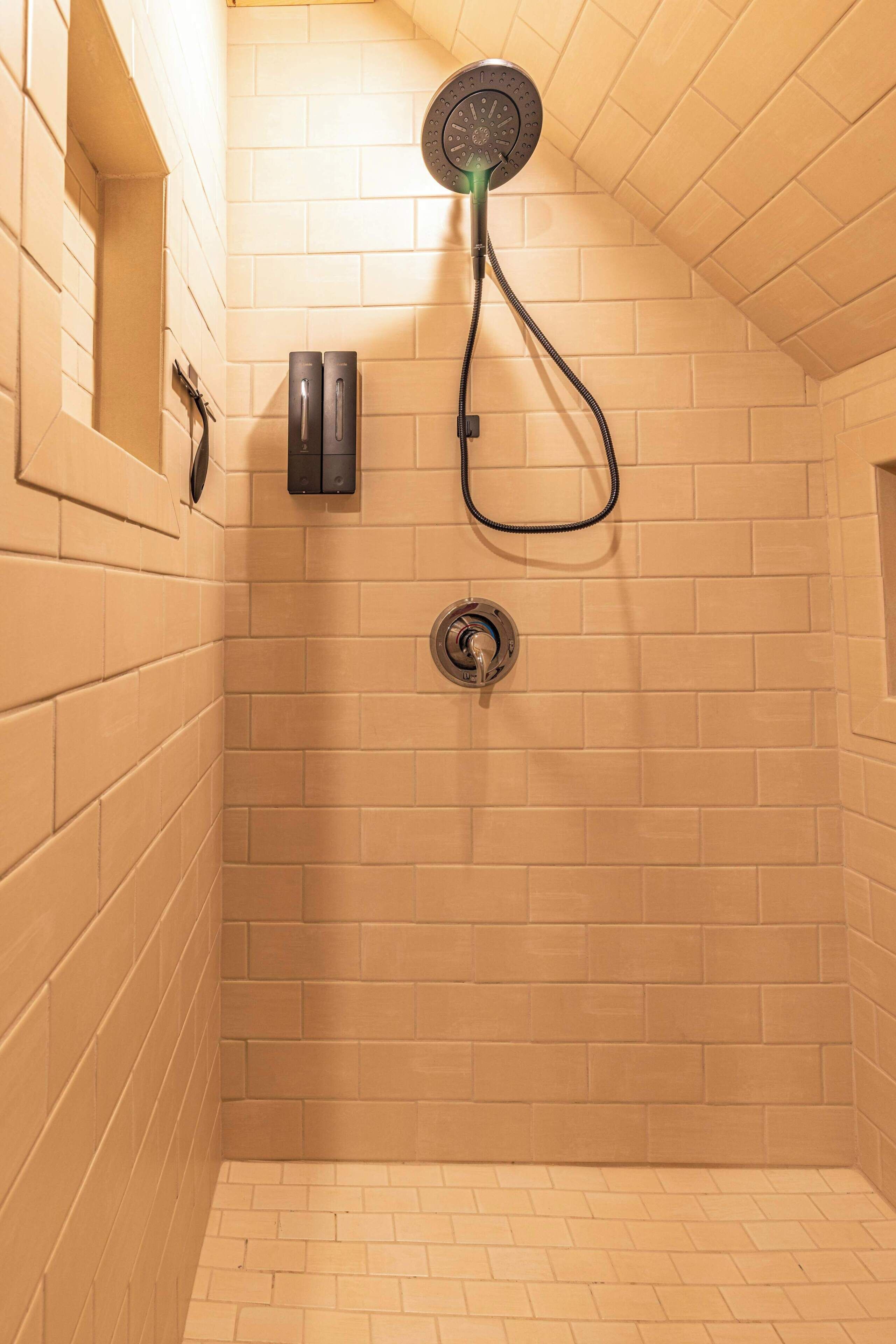 A shower with a handheld showerhead, a wall-mounted control panel, and a floor drain.