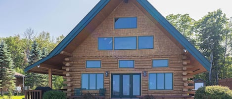 A log cabin with a gabled roof, multiple windows, and a front porch with benches.