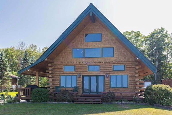 A log cabin with a gabled roof, multiple windows, and a front porch with benches.