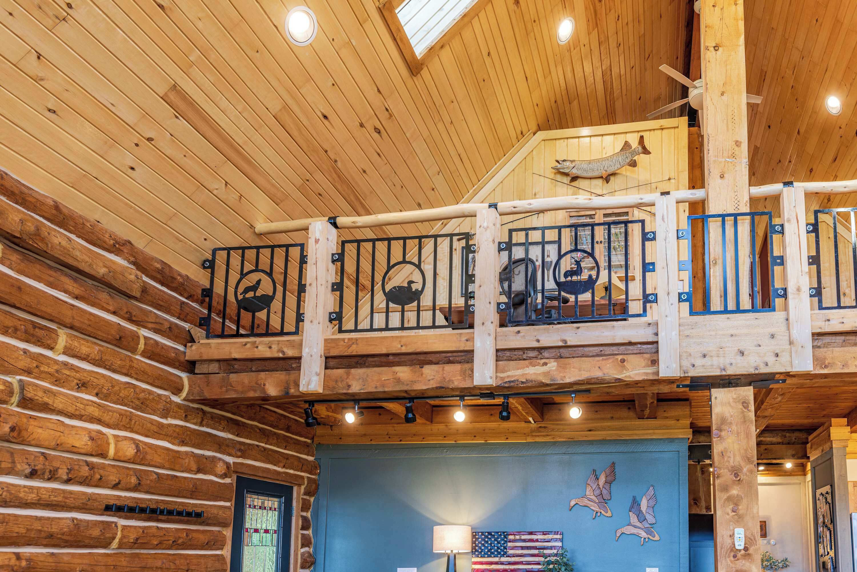 A wooden interior with a balcony, a ceiling fan, and a wall with a flag and bird artwork.