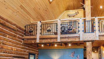 A wooden interior with a balcony, a ceiling fan, and a wall with a flag and bird artwork.