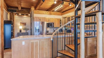 A spacious kitchen with wooden cabinetry, a central island, and a staircase leading to an upper level.