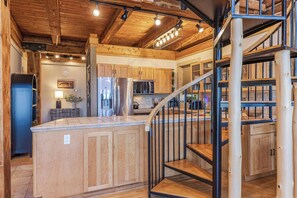 A spacious kitchen with wooden cabinetry, a central island, and a staircase leading to an upper level.